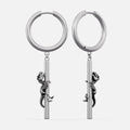 Silver-tone hoop earrings with a dangling dinosaur skeleton charm climbing a bar, shown as a pair