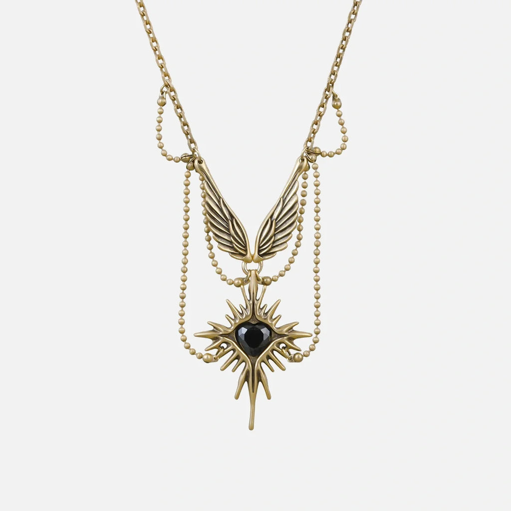 Gold-tone necklace featuring layered chains, wings and a starburst pendant with black stone, laid flat on white background