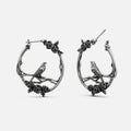 Pair of oxidized silver-tone hoop earrings with rose vine and perched bird design, front view