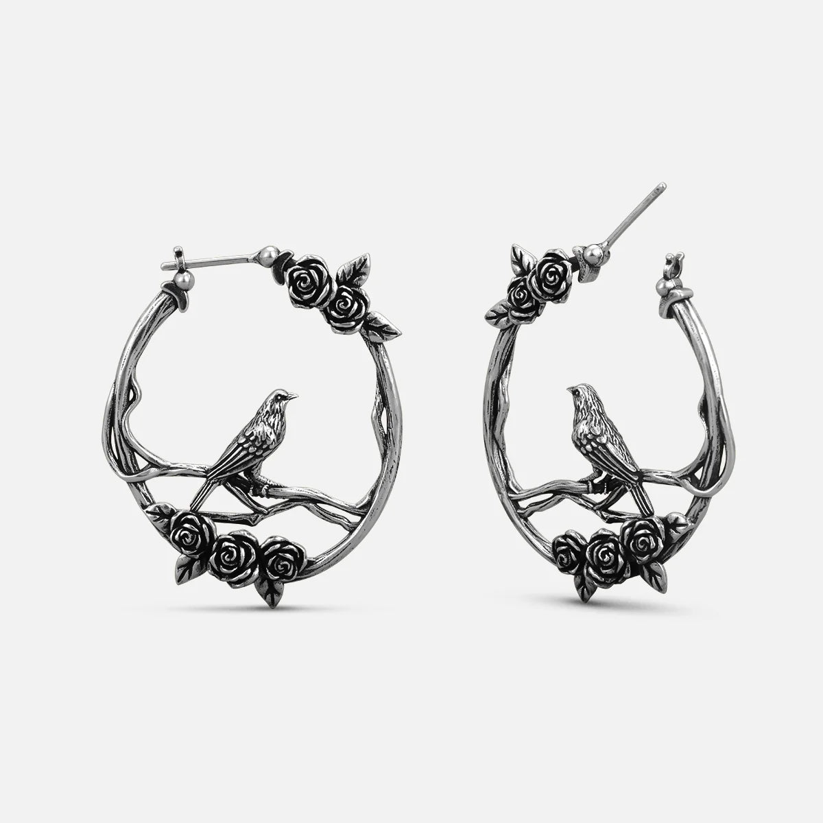 Pair of oxidized silver-tone hoop earrings with rose vine and perched bird design, front view
