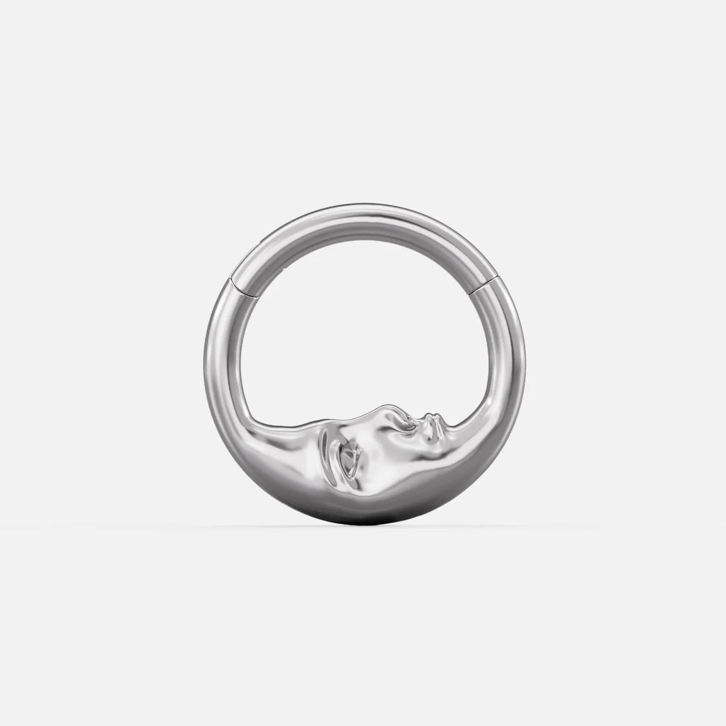 Titanium clicker ring with a sculpted serene face design, front view on a plain background